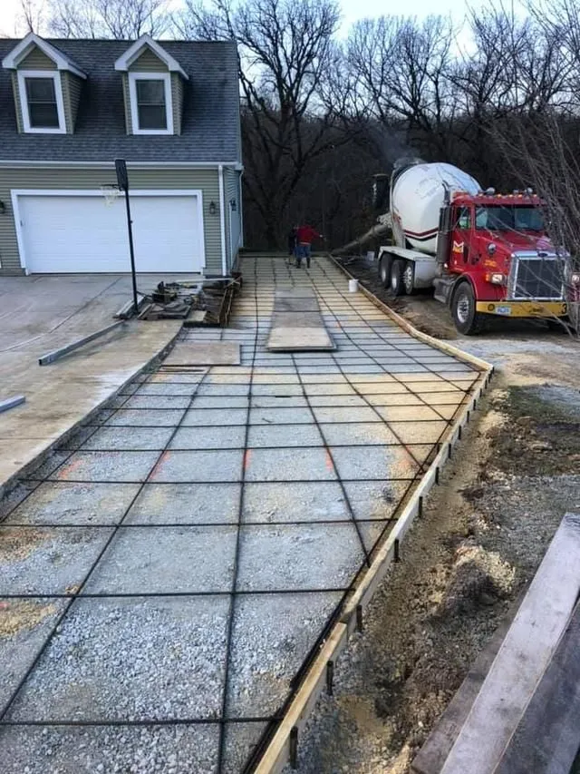 Red concrete truck pouring a new driveway over a rebar grid in front of a two-car garage