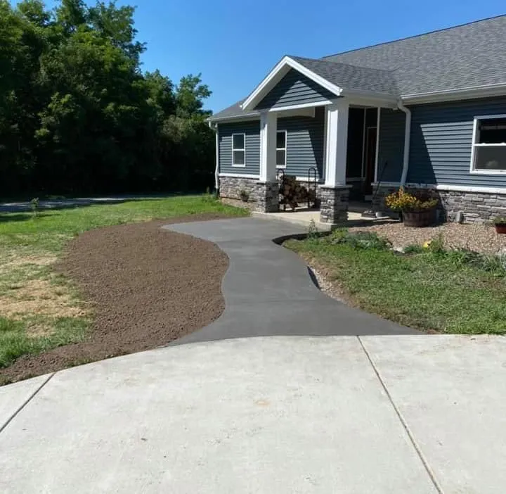 A concrete walkway curves toward a blue-sided house with a porch and gray roof.