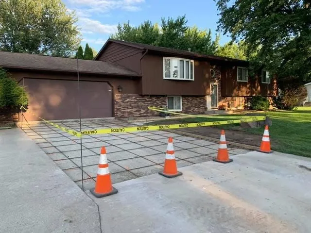 Driveway forms and rebar grid set inside caution tape and orange cones at a brown split-level home
