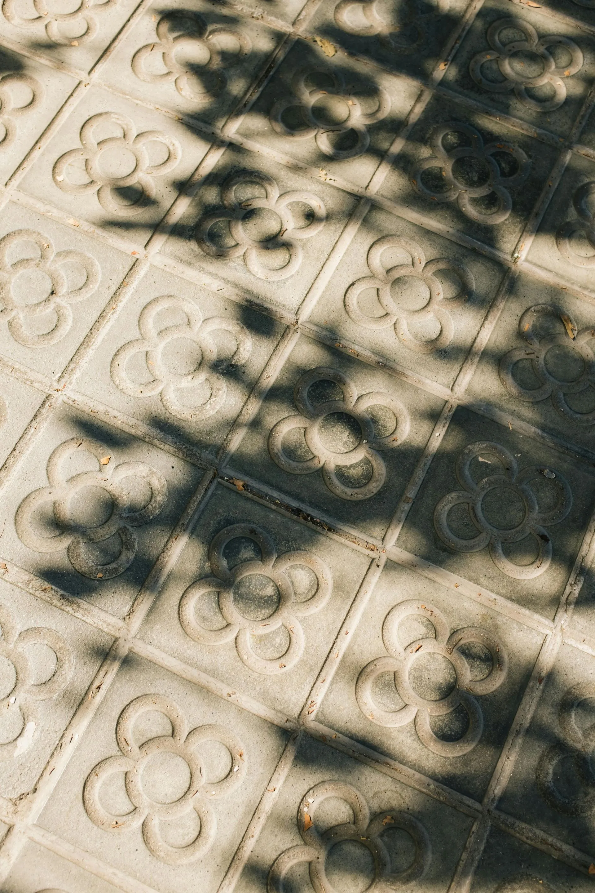 Pale paving with a pressed floral tile pattern in dappled tree shade