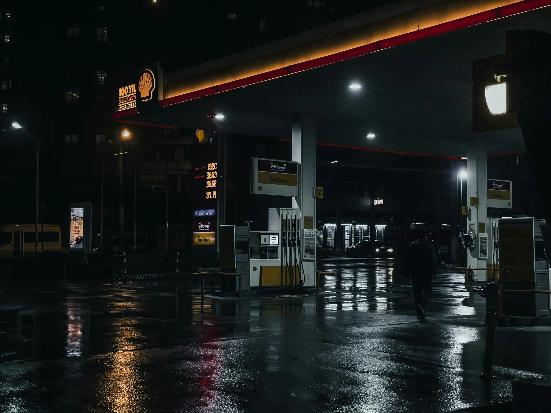 Wet gas station forecourt reflecting canopy lights and fuel pumps at night