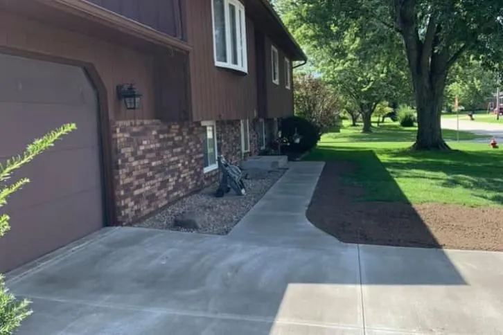 Brown house with brick facade, concrete walkway, green lawn, sunny day.