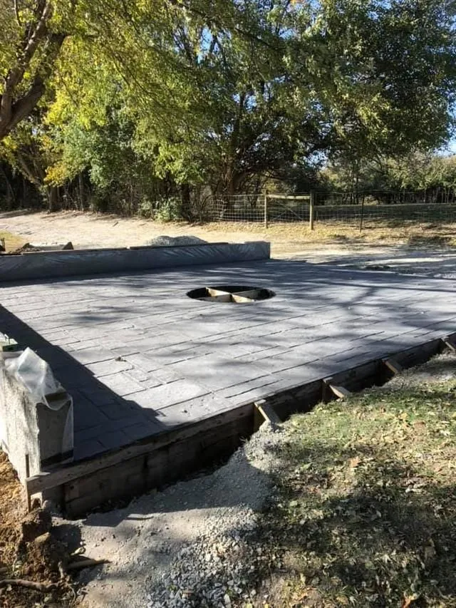 Concrete pad with a circular opening, surrounded by wooden forms, in an outdoor setting.