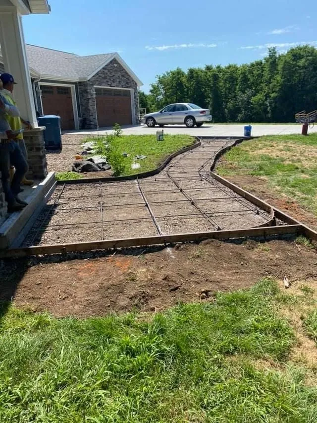Concrete walkway under construction in front of a house. Rebar and wooden forms are visible.