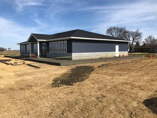 Blue building with a dark roof and a concrete sidewalk, located in a dirt lot.