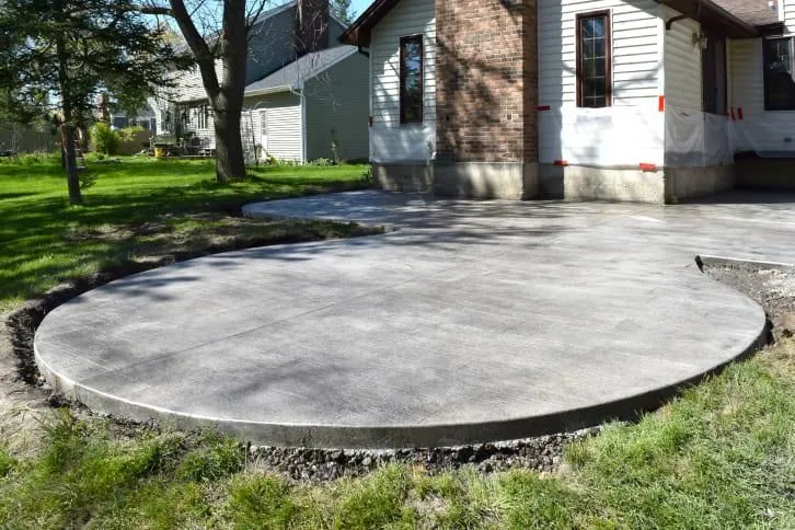 Workers smoothing wet concrete for a sidewalk with hand tools in an outdoor setting.
