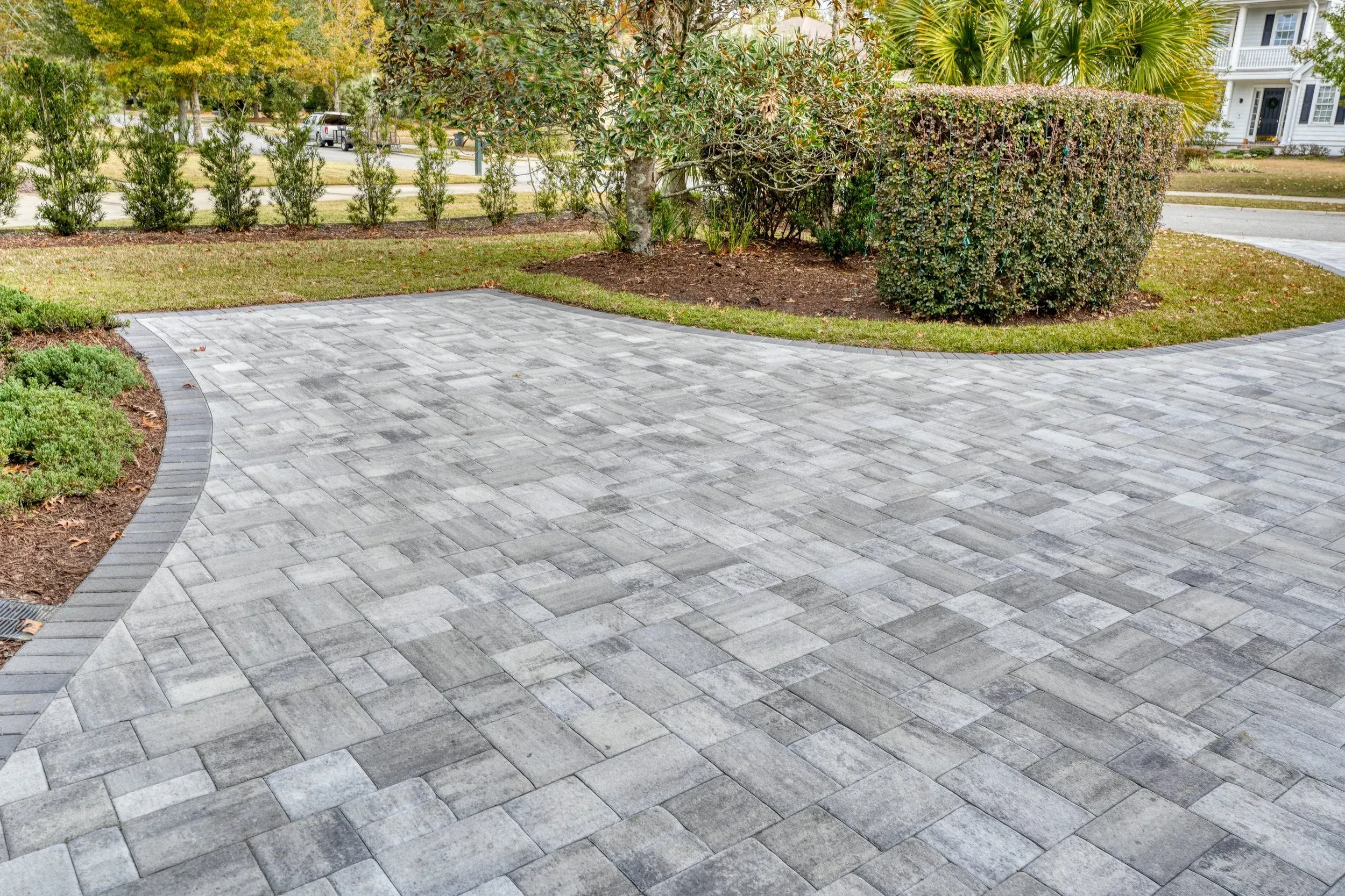 Grey paver driveway curving around a landscaped yard with shrubs and trees