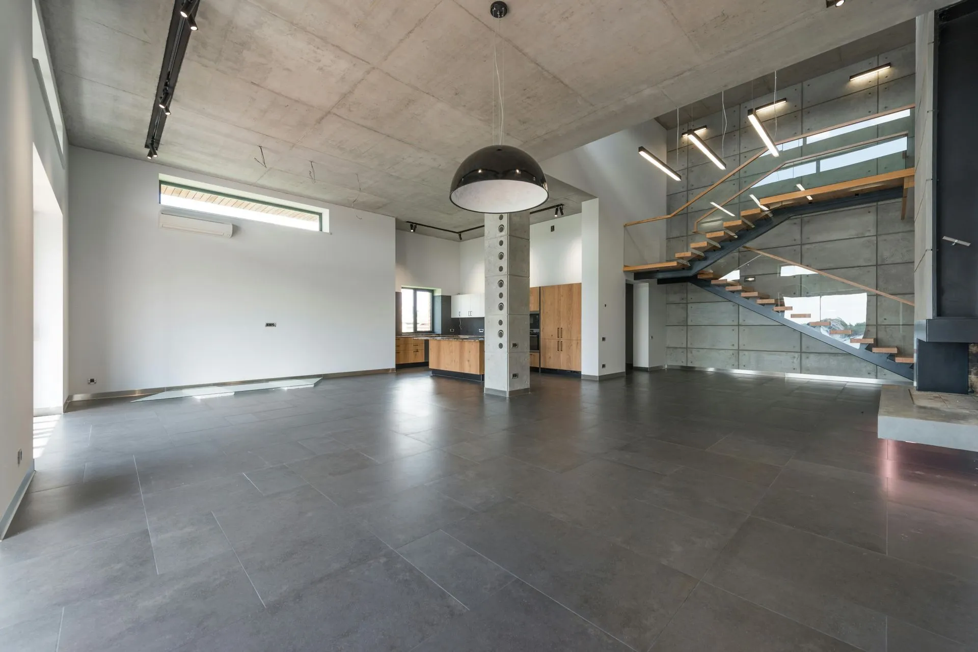 Open modern interior with a large-format grey concrete floor and a floating staircase