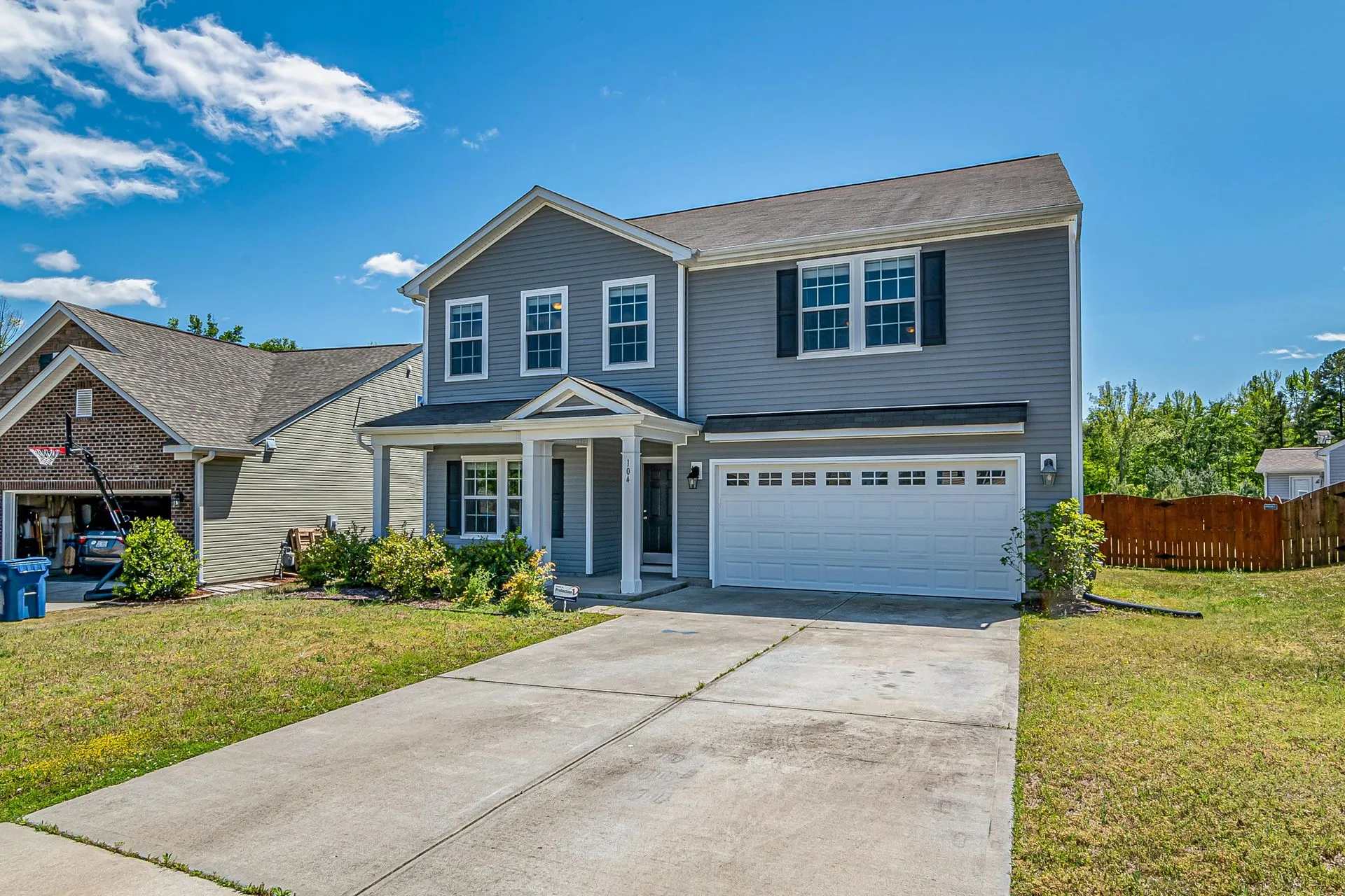Two-story gray house with a wide concrete driveway and front lawn on a sunny day